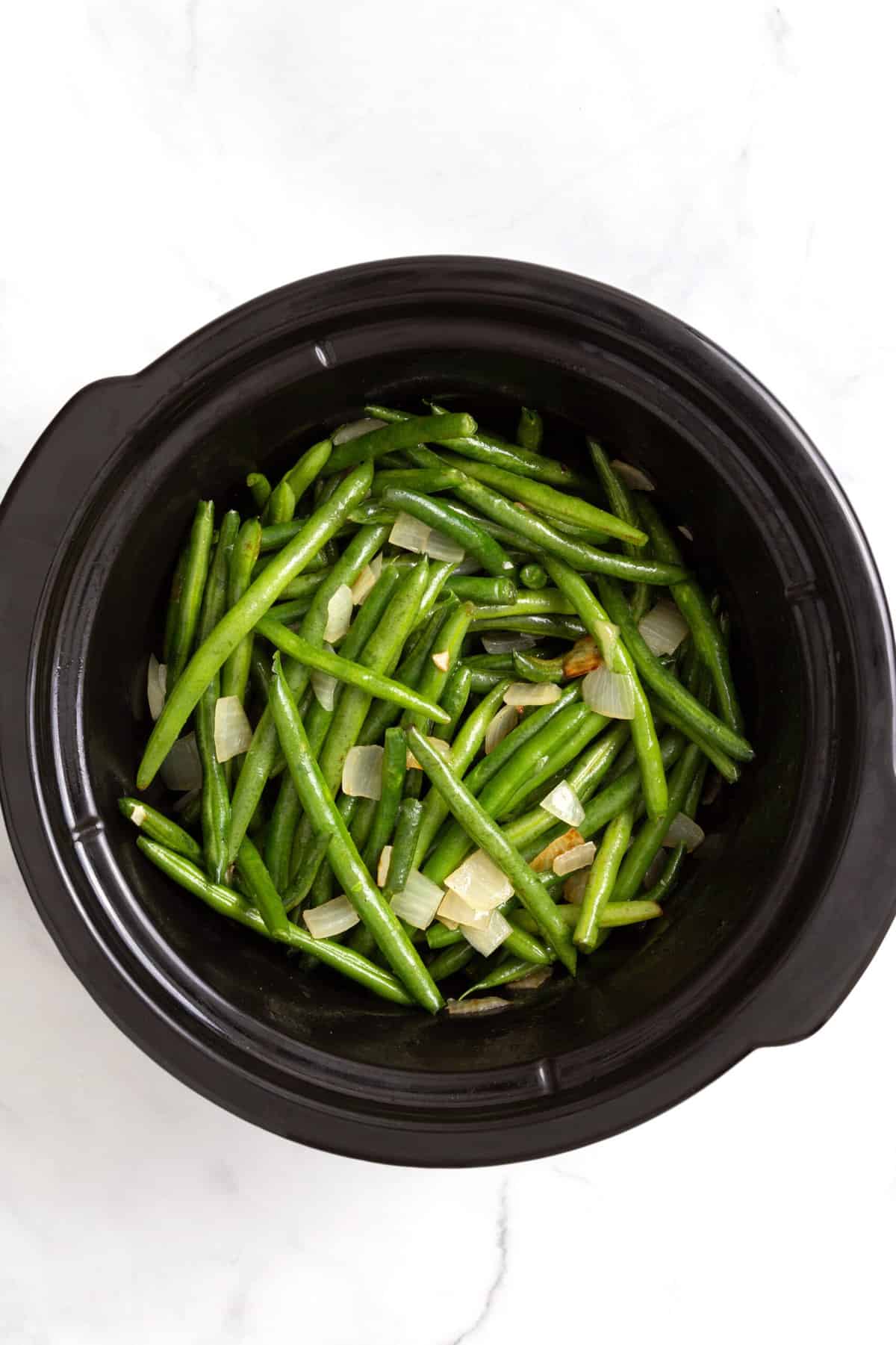 top down image of green beans cooking in a slow cooker. 
