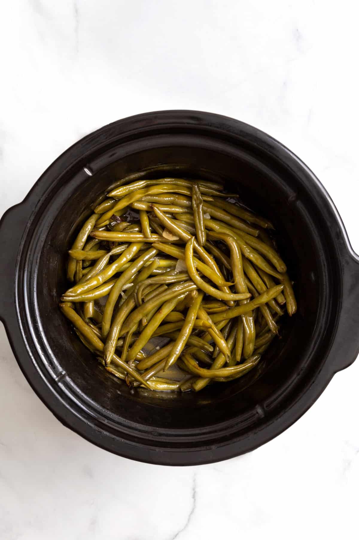 top down image of green beans cooking in a slow cooker. 