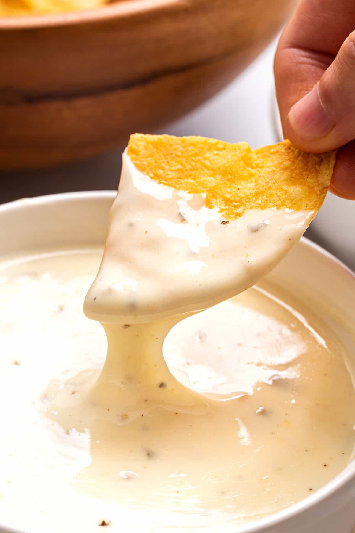 close up image of a tortilla chip dipping into velvetta queso blanco in a slow cooker. 