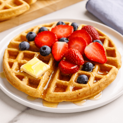 A buttermilk waffle topped with strawberries, blueberries, butter, and syrup.