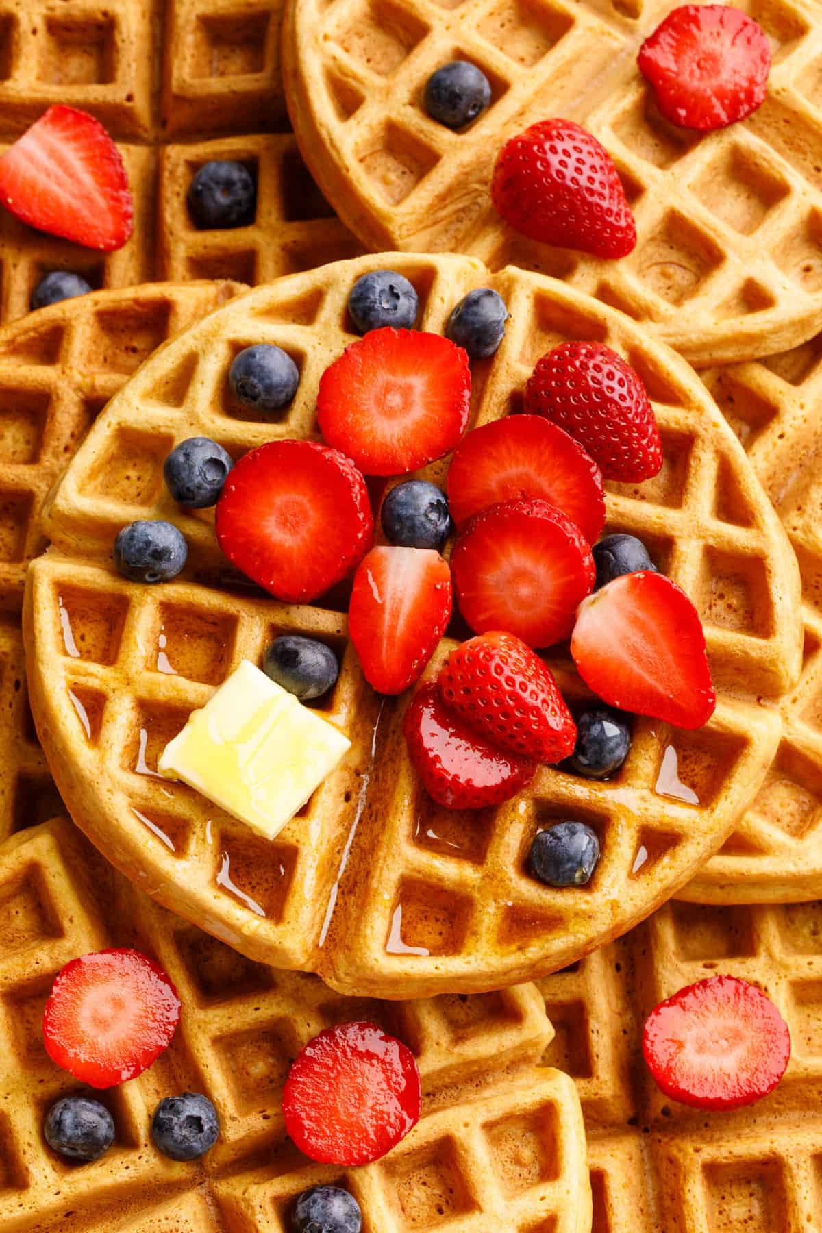 top down image of buttermilk waffles topped with fresh blueberries and strawberries, syrup and a slab of butter. 