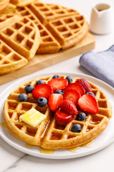 A buttermilk waffle topped with strawberries, blueberries, butter, and syrup.