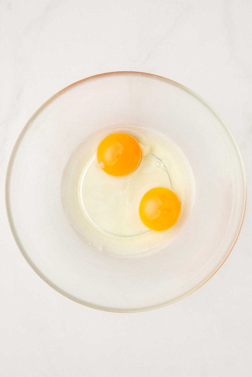 2 raw eggs in a large glass bowl.