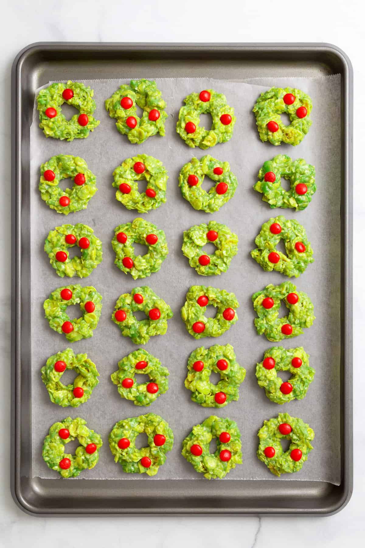 24 Christmas Wreath Cornflake Cookies arranged on a parchment-lined baking tray. 