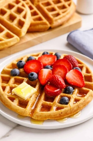 A buttermilk waffle topped with strawberries, blueberries, butter, and syrup.