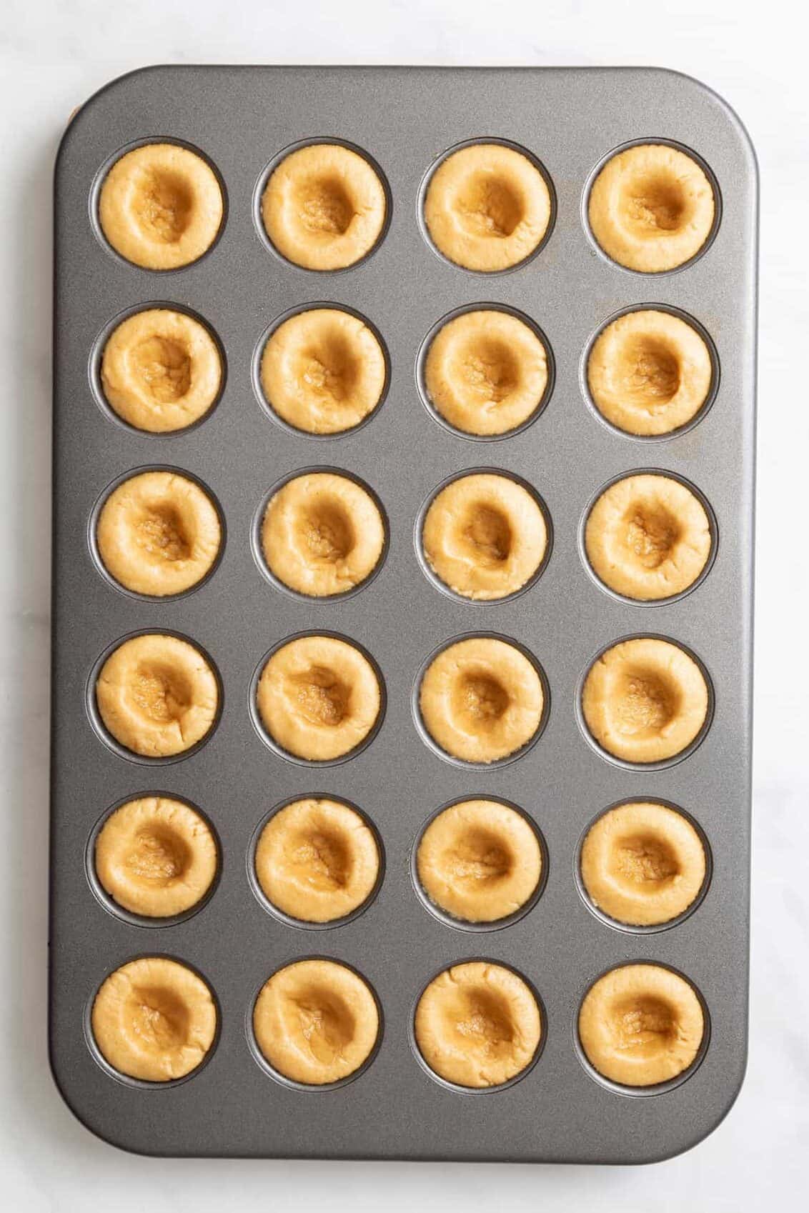 top down image of a 24-mini muffin tin with peanut butter cookie pressed in each spot.