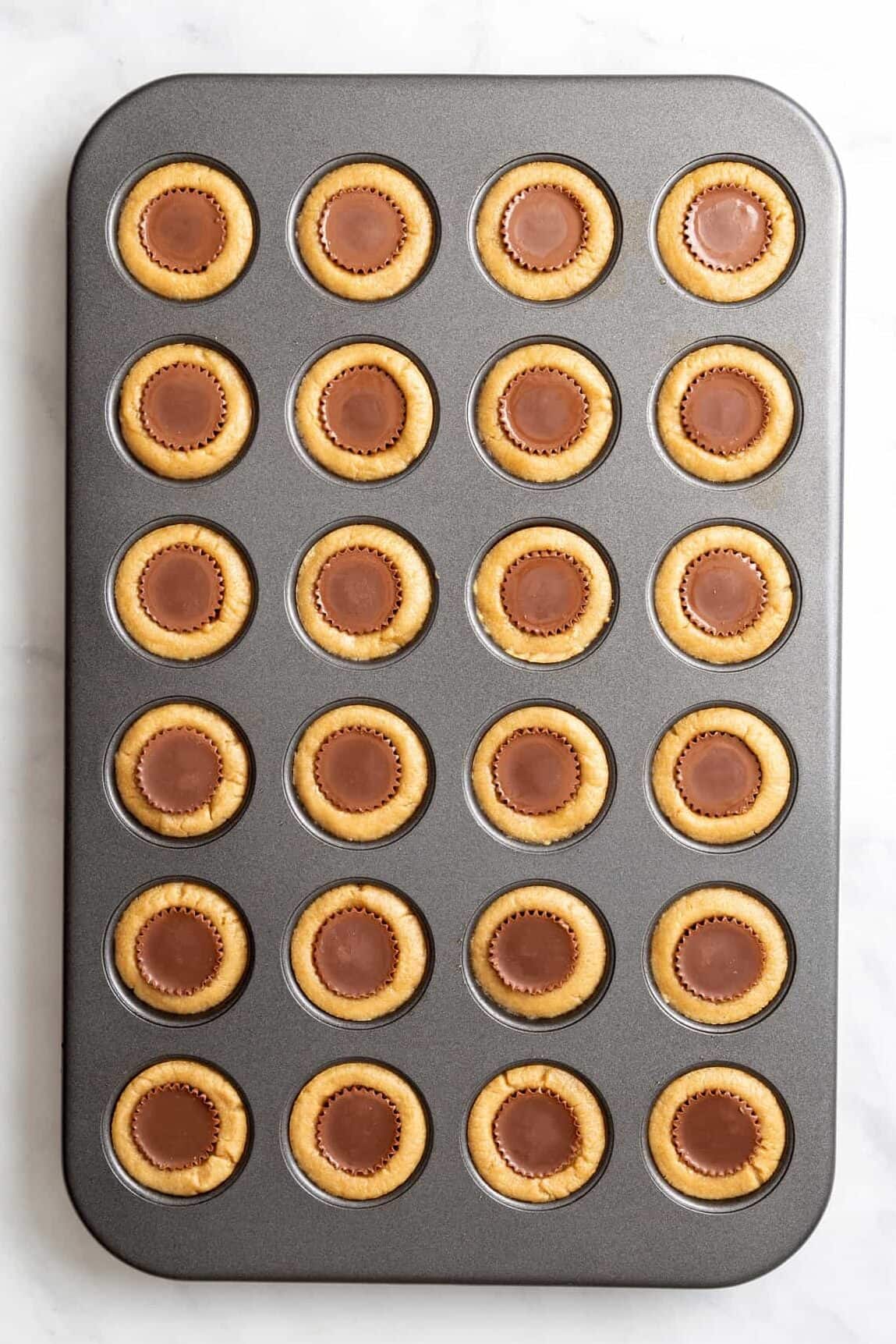 top down image of a 24-mini muffin tin with peanut butter cookie pressed in each spot and filled with a reese's peanut butter cup. 
