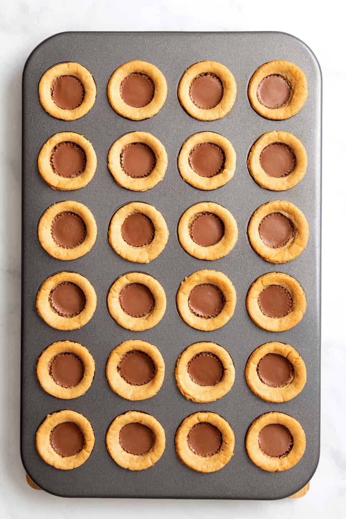 top down image of a 24-mini muffin tin with peanut butter cookie pressed in each spot and filled with a reese's peanut butter cup. 
