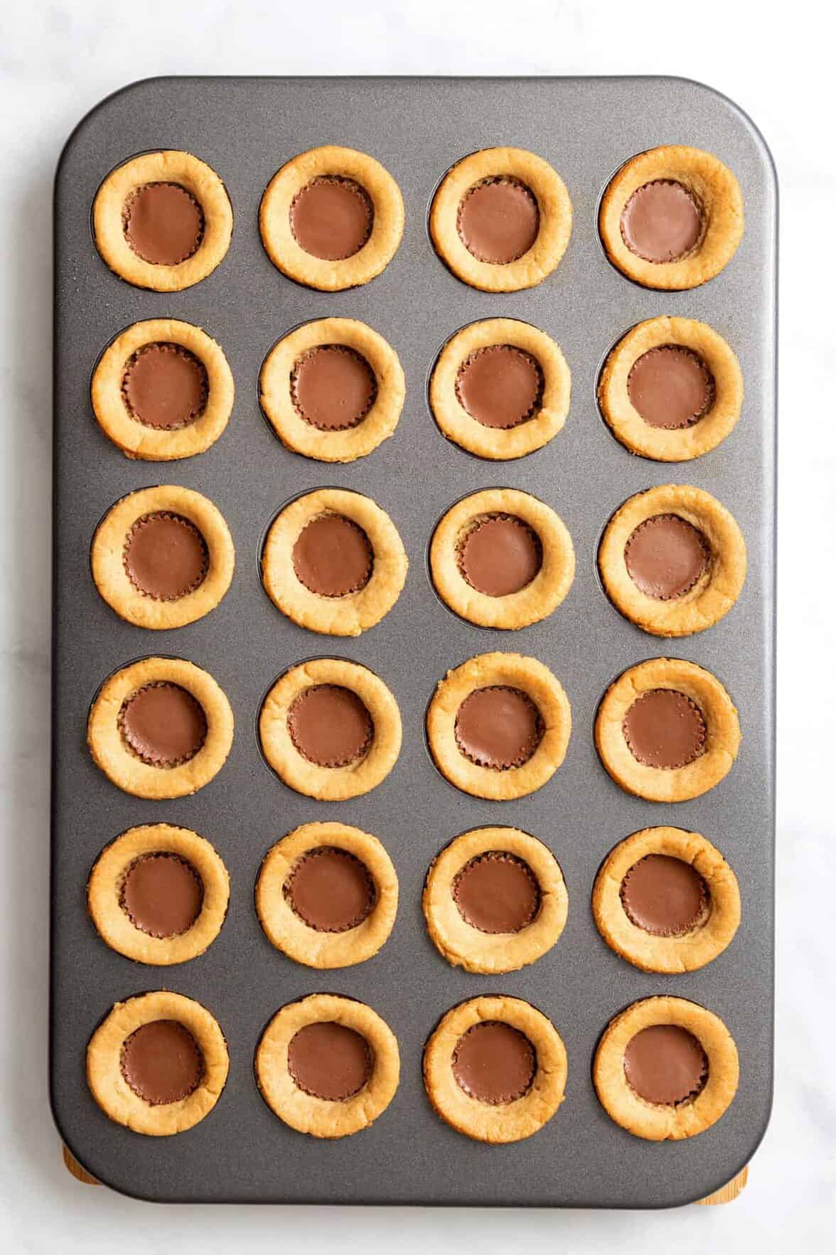 top down image of a 24-mini muffin tin with peanut butter cookie pressed in each spot and filled with a reese's peanut butter cup.