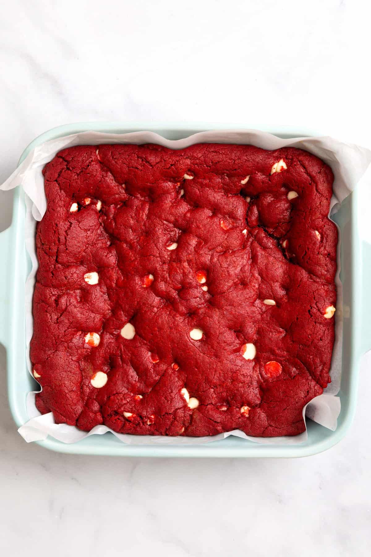 baked red velvet brownies batter with white chocolate chips in an 8x8 blue ceramic baking dish. 