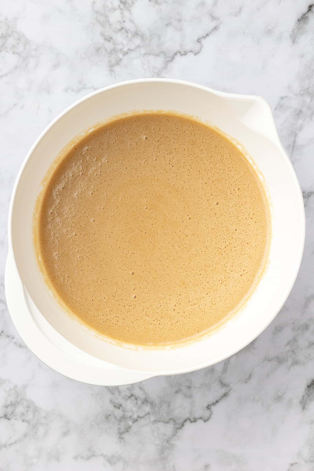 top down image of a white mixing bowl with combined flour, cornstarch, baking powder, salt, brown sugar, melted butter, eggs and vanilla extract. 