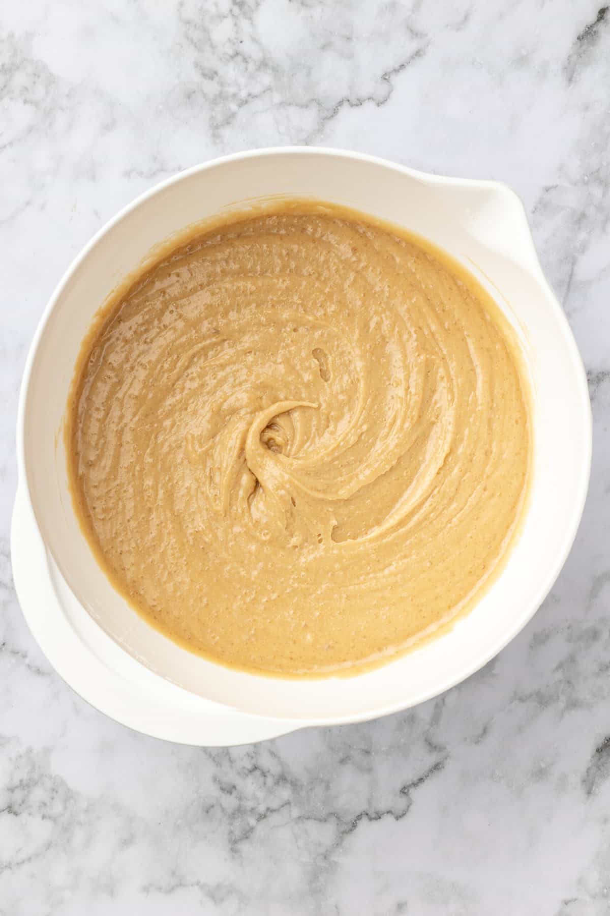 top down image of a white mixing bowl with combined flour, cornstarch, baking powder, salt, brown sugar, melted butter, eggs and vanilla extract. 