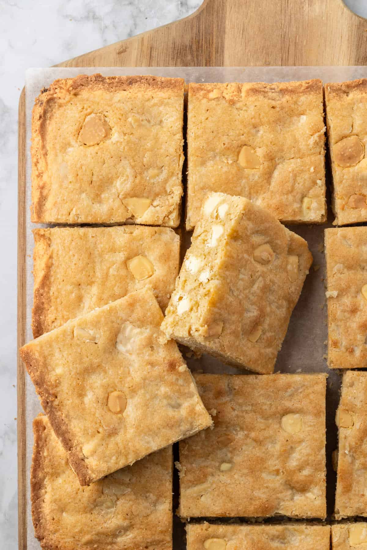 top down image of blonde brownies cut into squares sitting on top of parchment paper and a cutting board. 