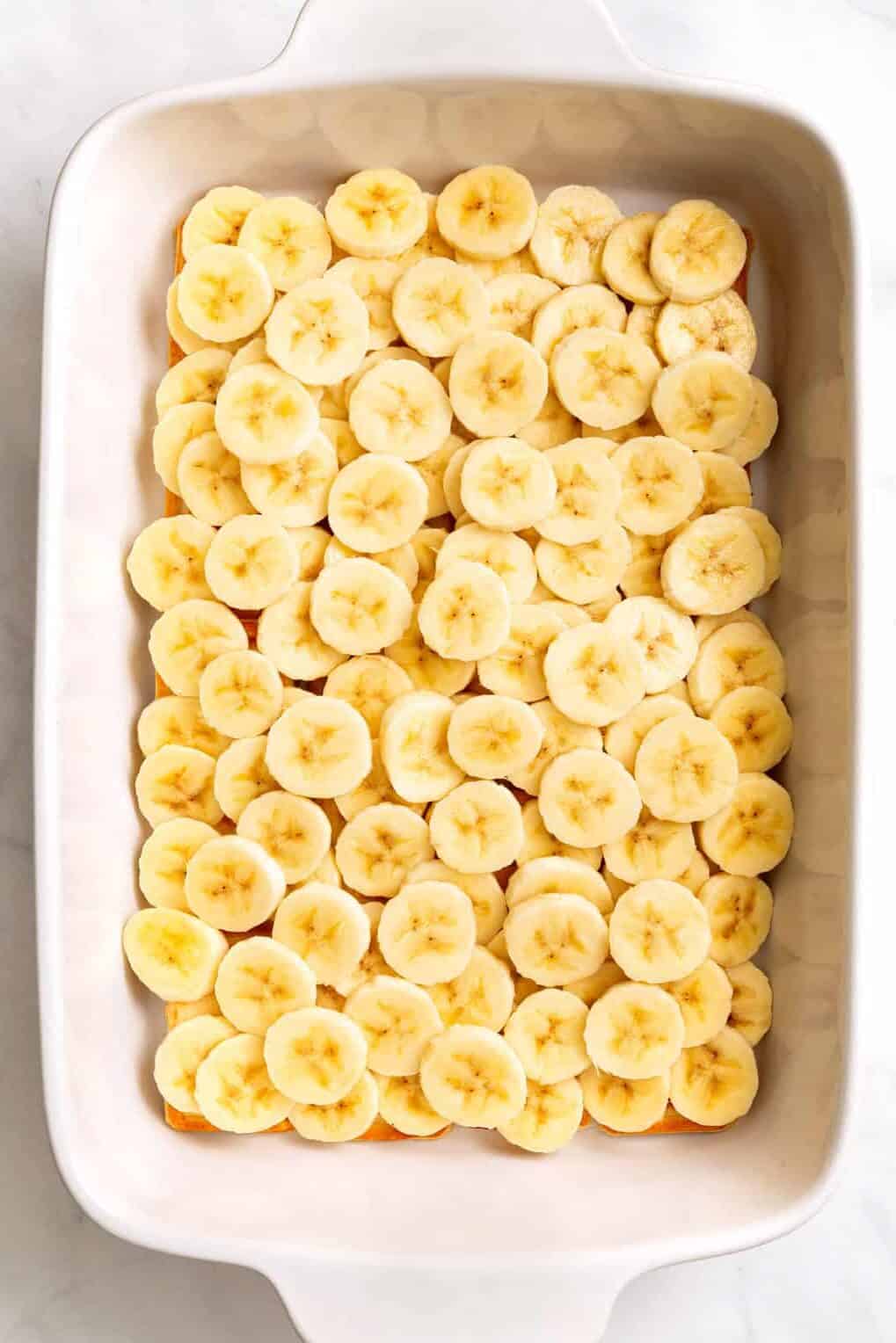 top down image of slice bananas sitting at the bottom of a 9x13 inch casserole dish.