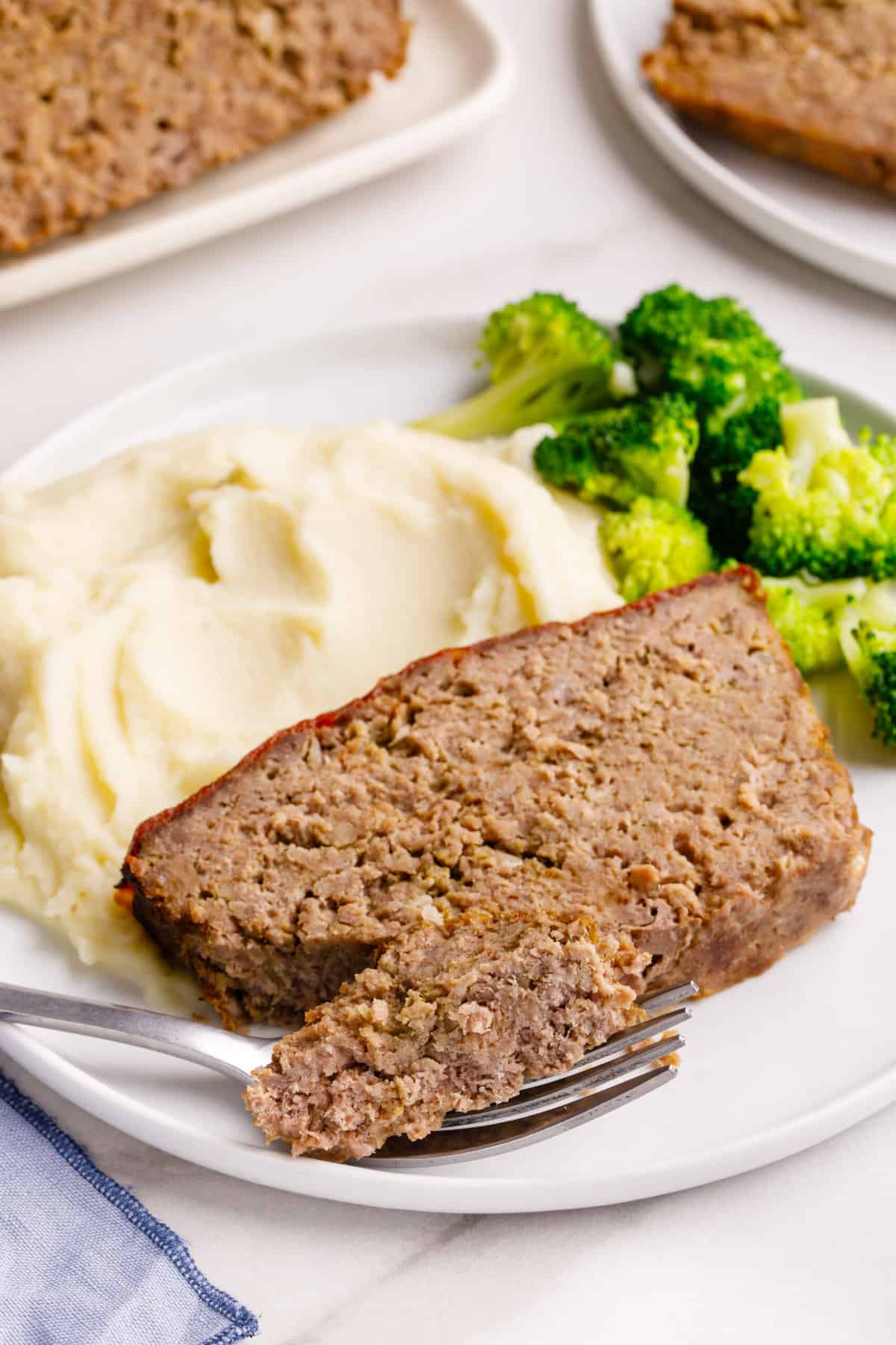 close up image of a plate of a serving of cracker barrel meatloaf, mashed potatoes and steamed broccoli.