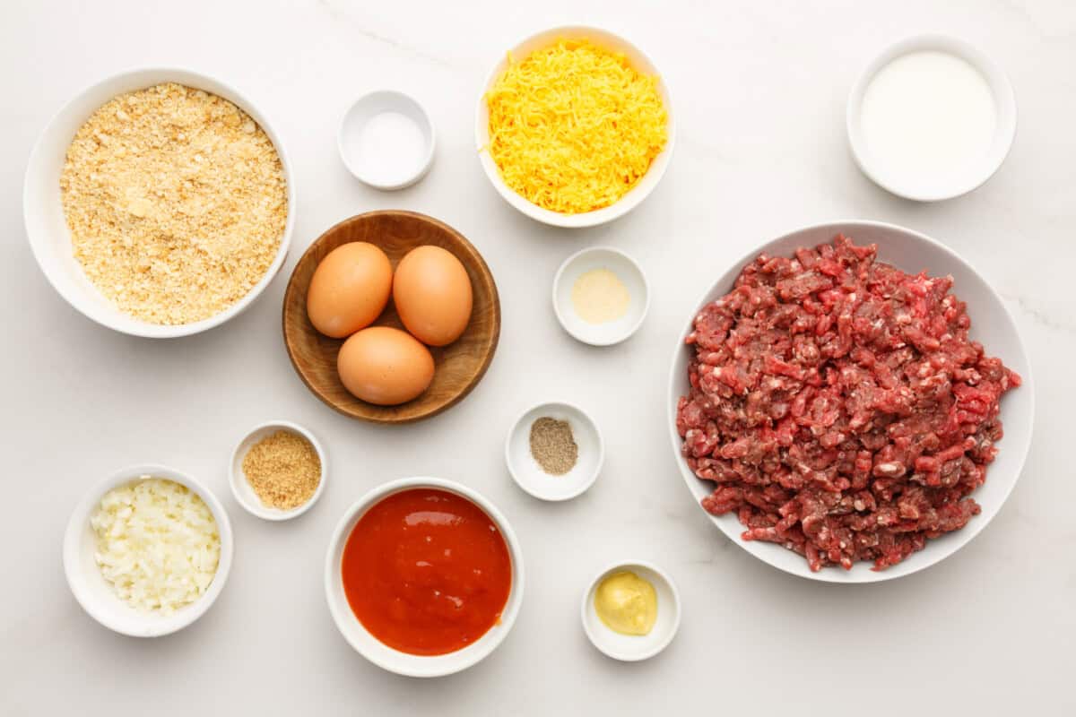 Ingredients for Cracker Barrel meatloaf recipe, including ground beef, ritz cracker crumbs,cheese, eggs, onions, and seasonings on a kitchen counter