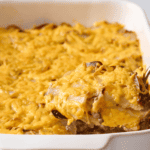 A spoon lifting a scoop of hamburger and potato casserole from a baking dish.