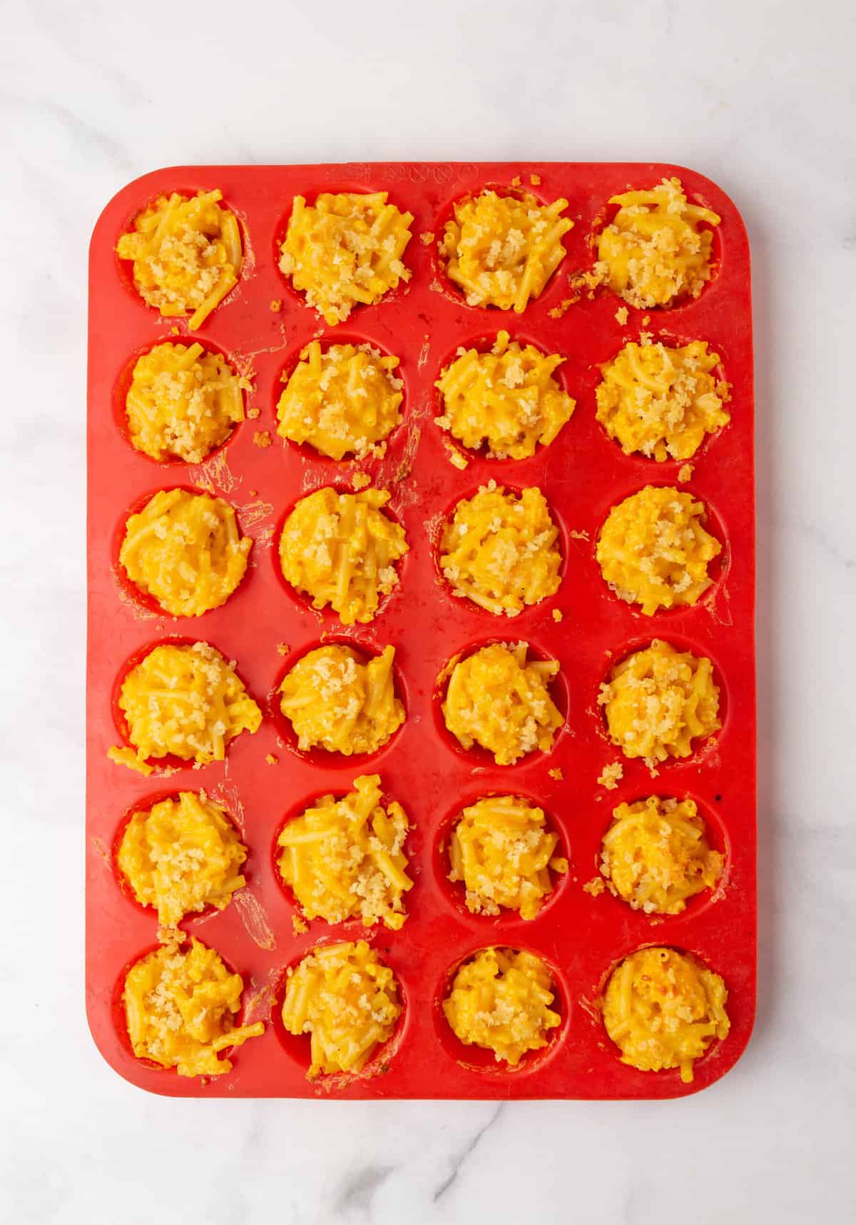 24 mac and cheese bites sitting in a red silicone mold. 