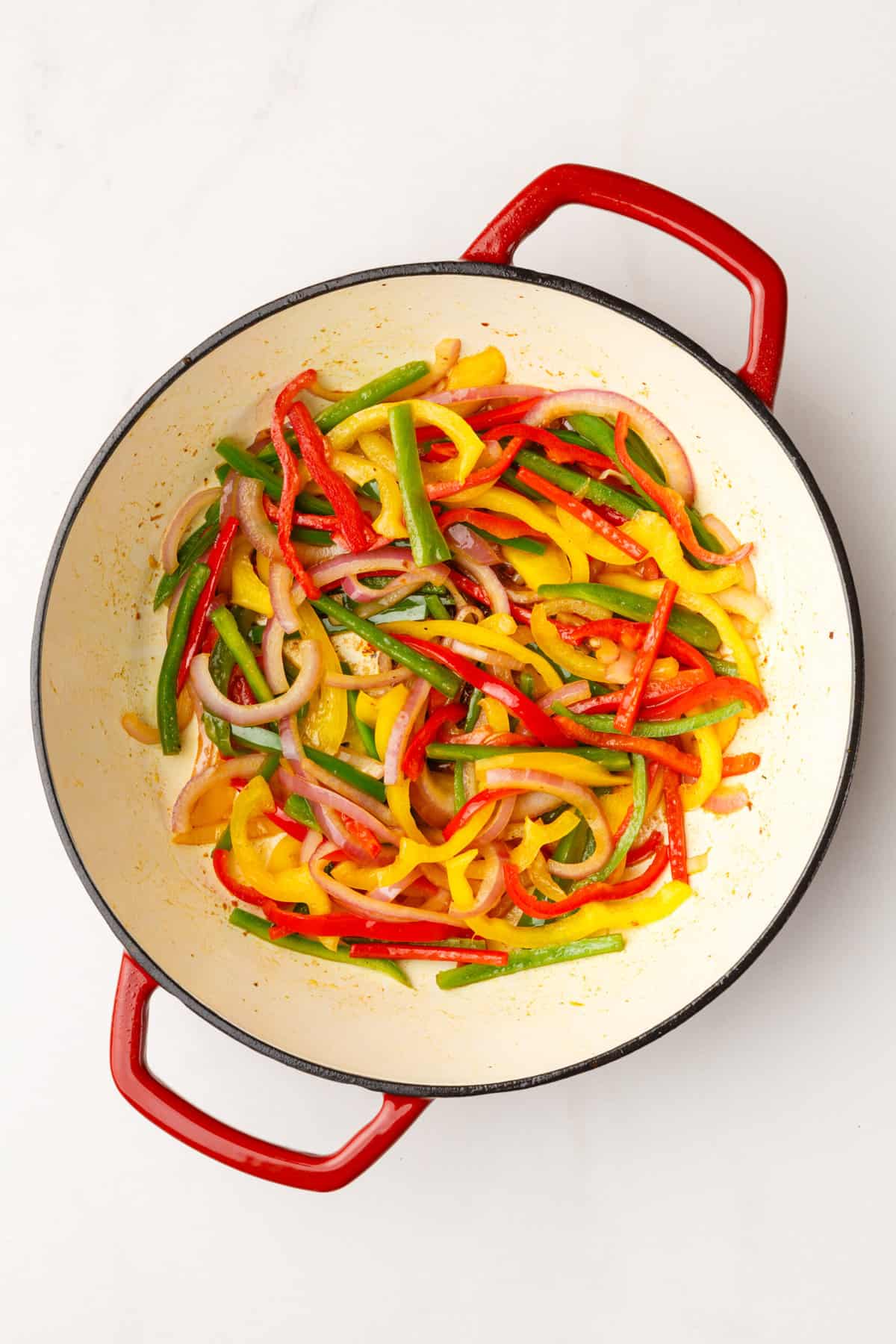 large dutch oven with cooked sliced bell peppers and red onion.