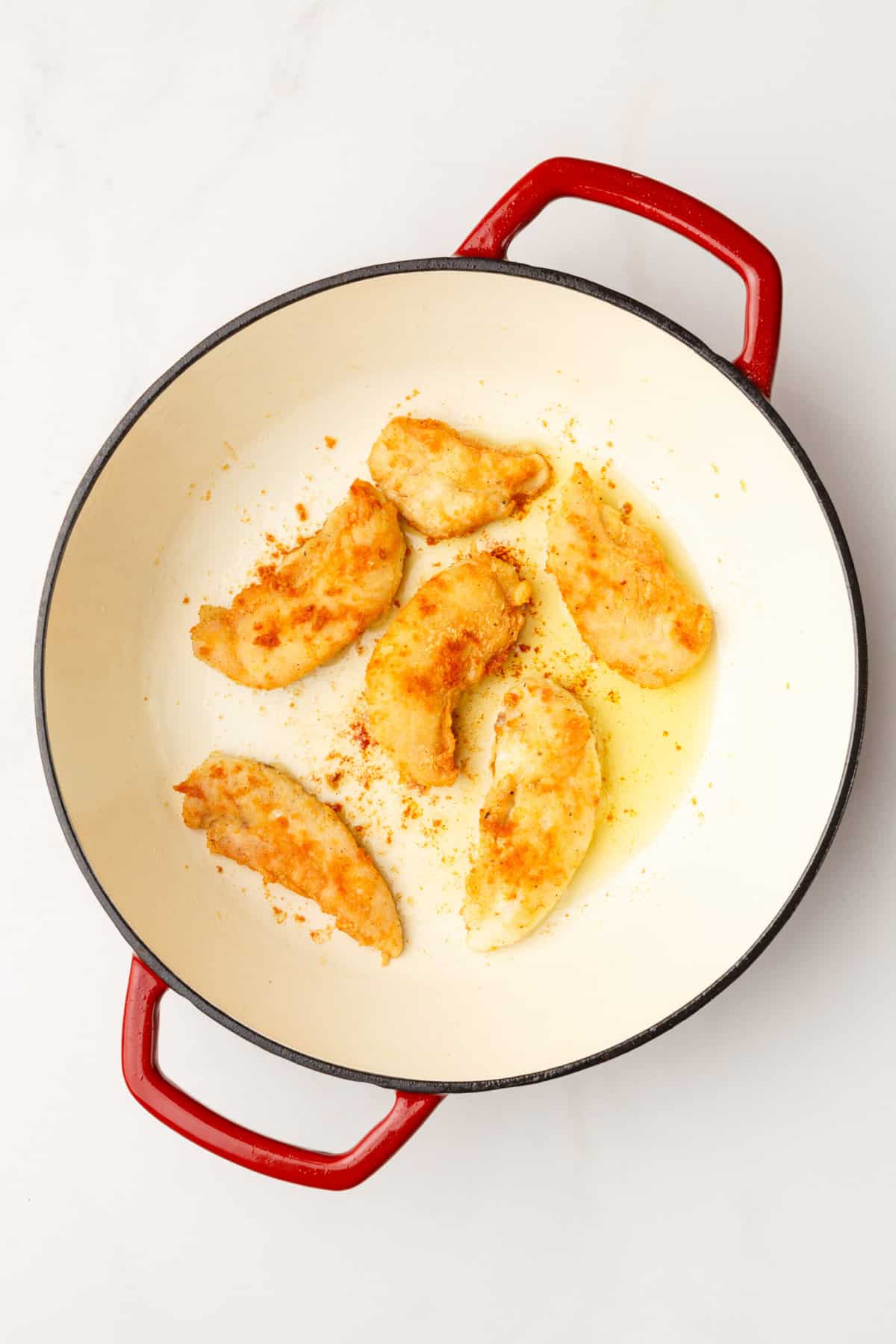 top down image of a large dutch oven with cooked chicken tenders. 