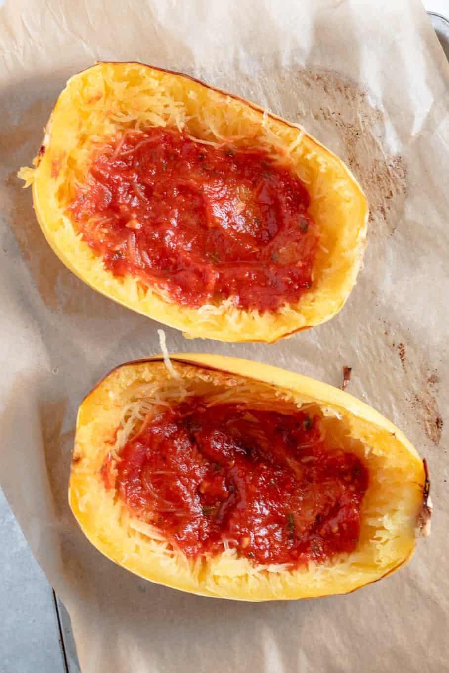 top down image of baked spaghetti squash with tomato sauce sitting on a parchment lined baking sheet.