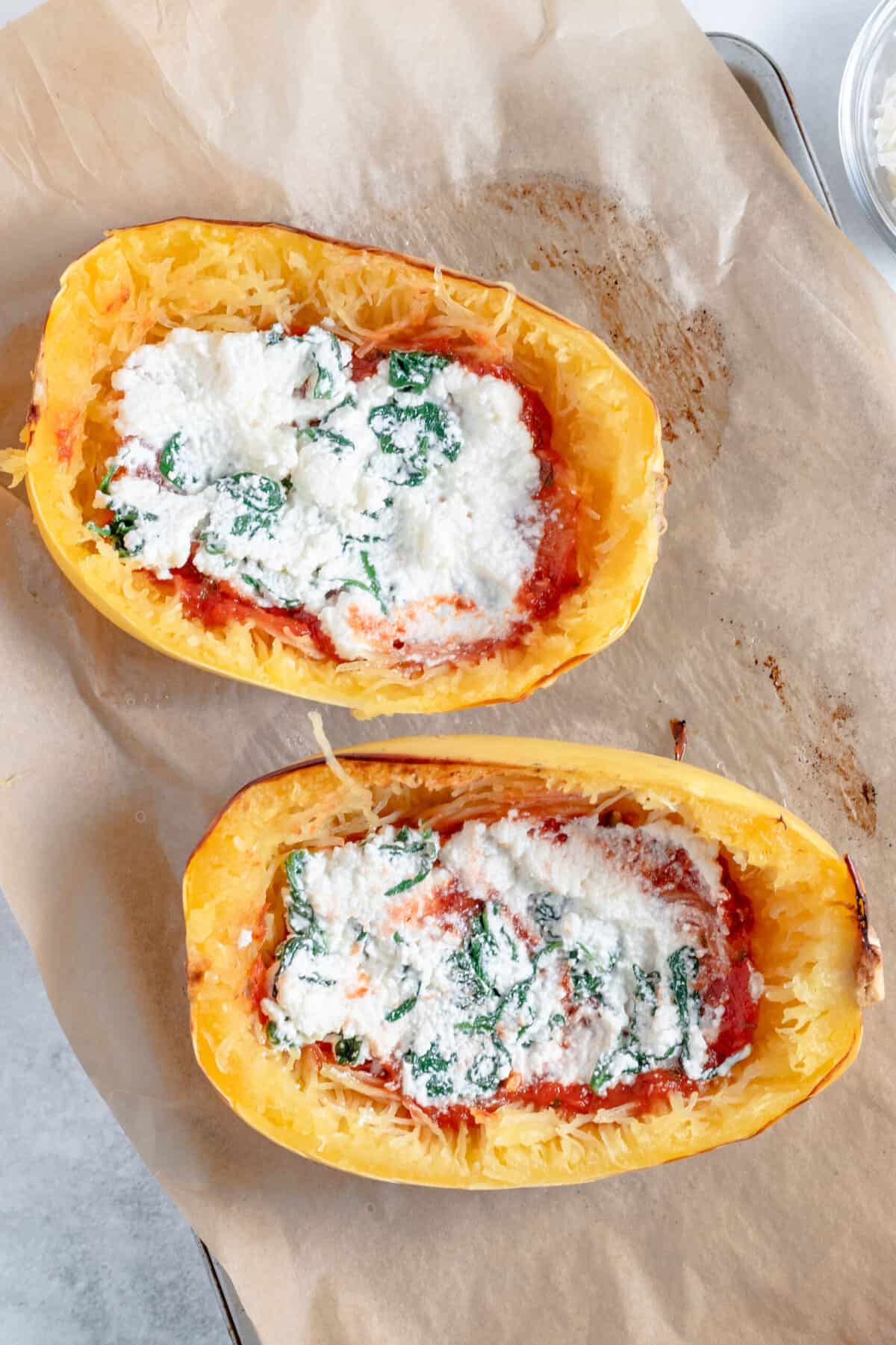 top down image of stuffed lasagna spaghetti squash sitting on a parchment lined baking sheet.