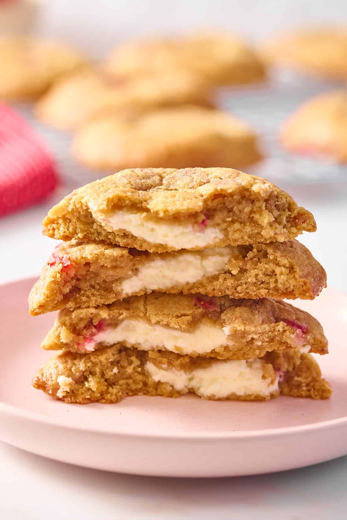 two strawberry cheesecake cookies cut in half and stacked to show the cream cheese filling, sitting on a pink round plate. 