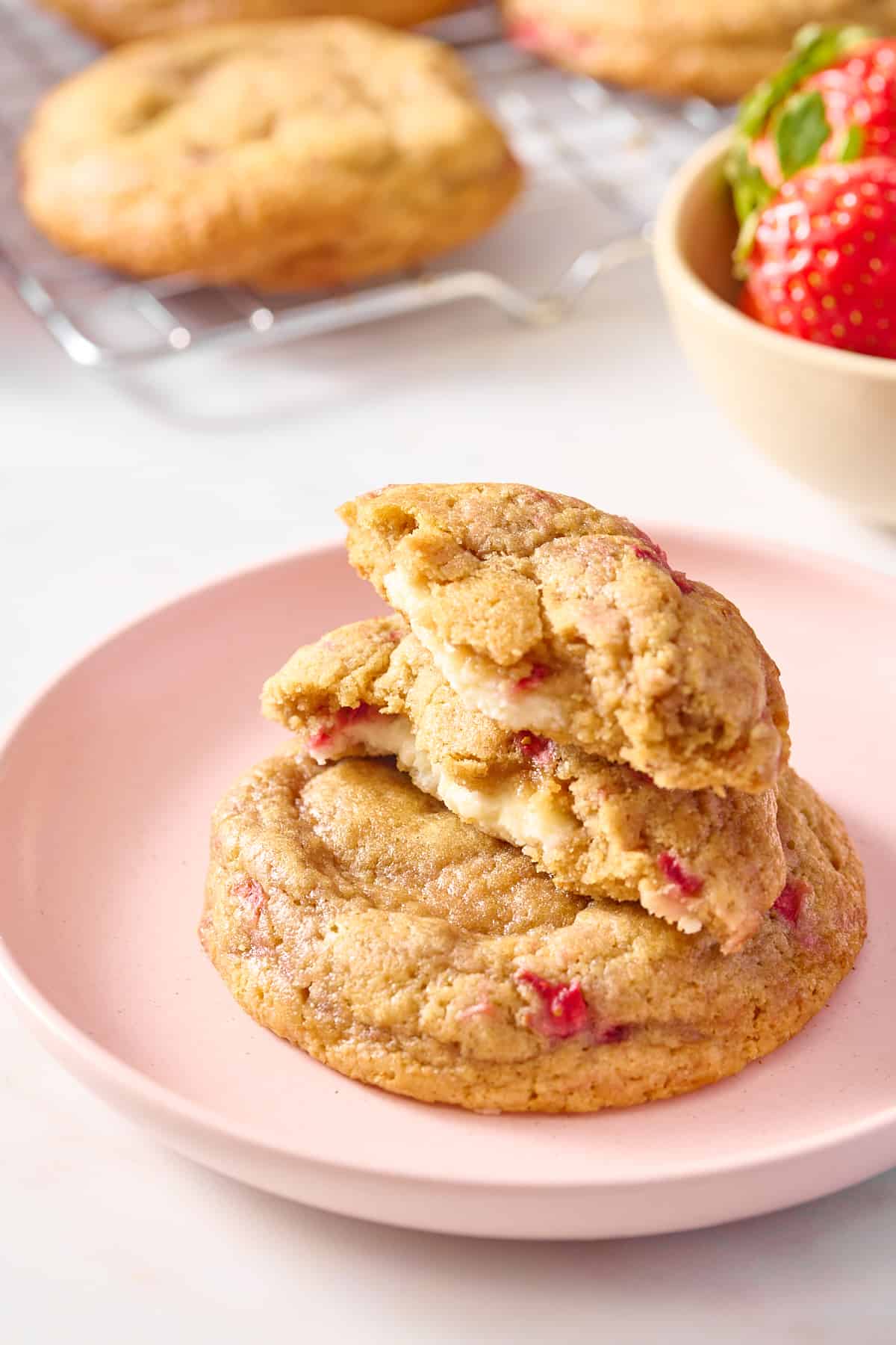two strawberry cheesecake cookies stacked and served on a pink round plate. 