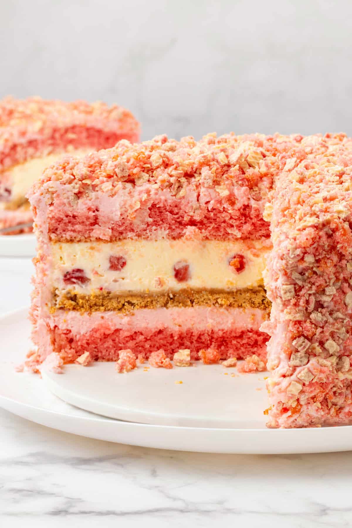 cross section of strawberry shortcake cheesecake sitting on a white round cake plate.