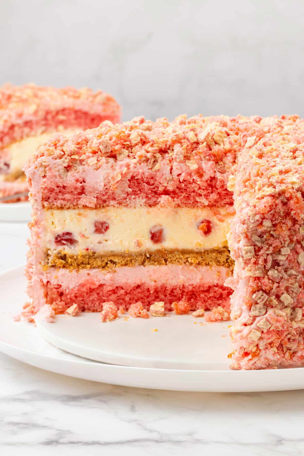 cross section of strawberry shortcake cheesecake sitting on a white round cake plate. 