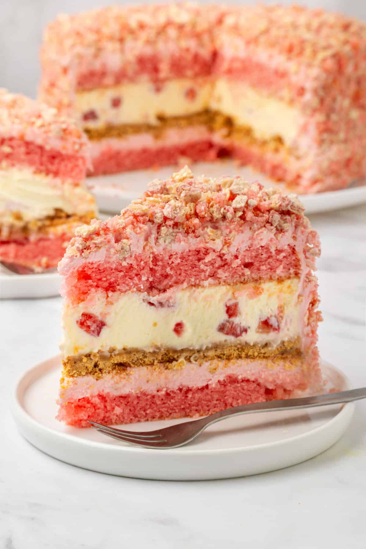 slice of strawberry shortcake cheesecake sitting on a white round plate with a silver fork. 