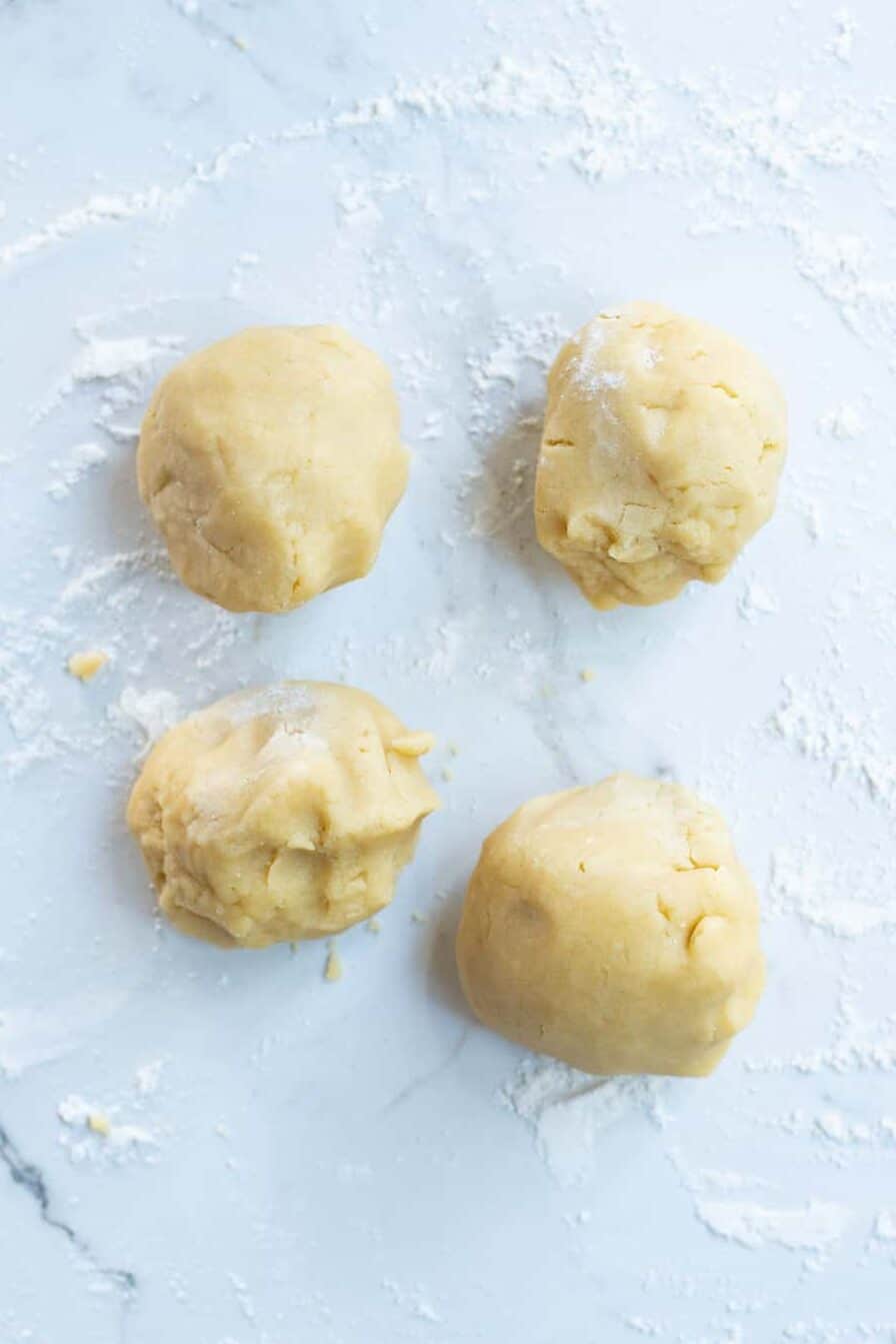 four sugar cookie dough balls sitting on a floured marble countertop.
