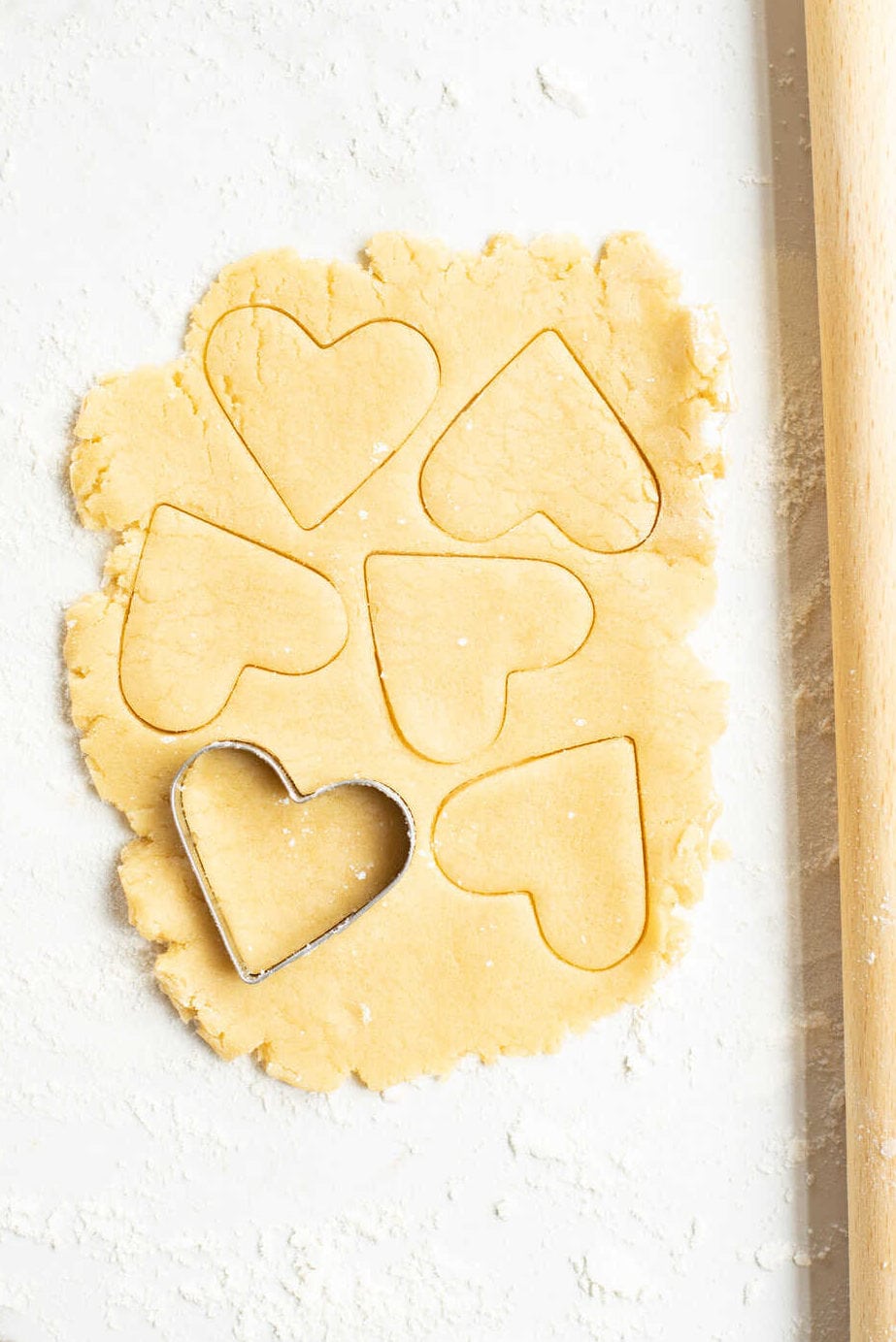 sugar cookie dough rolled out on a floured marble countertop with a heart-shaped cookie cutter. 