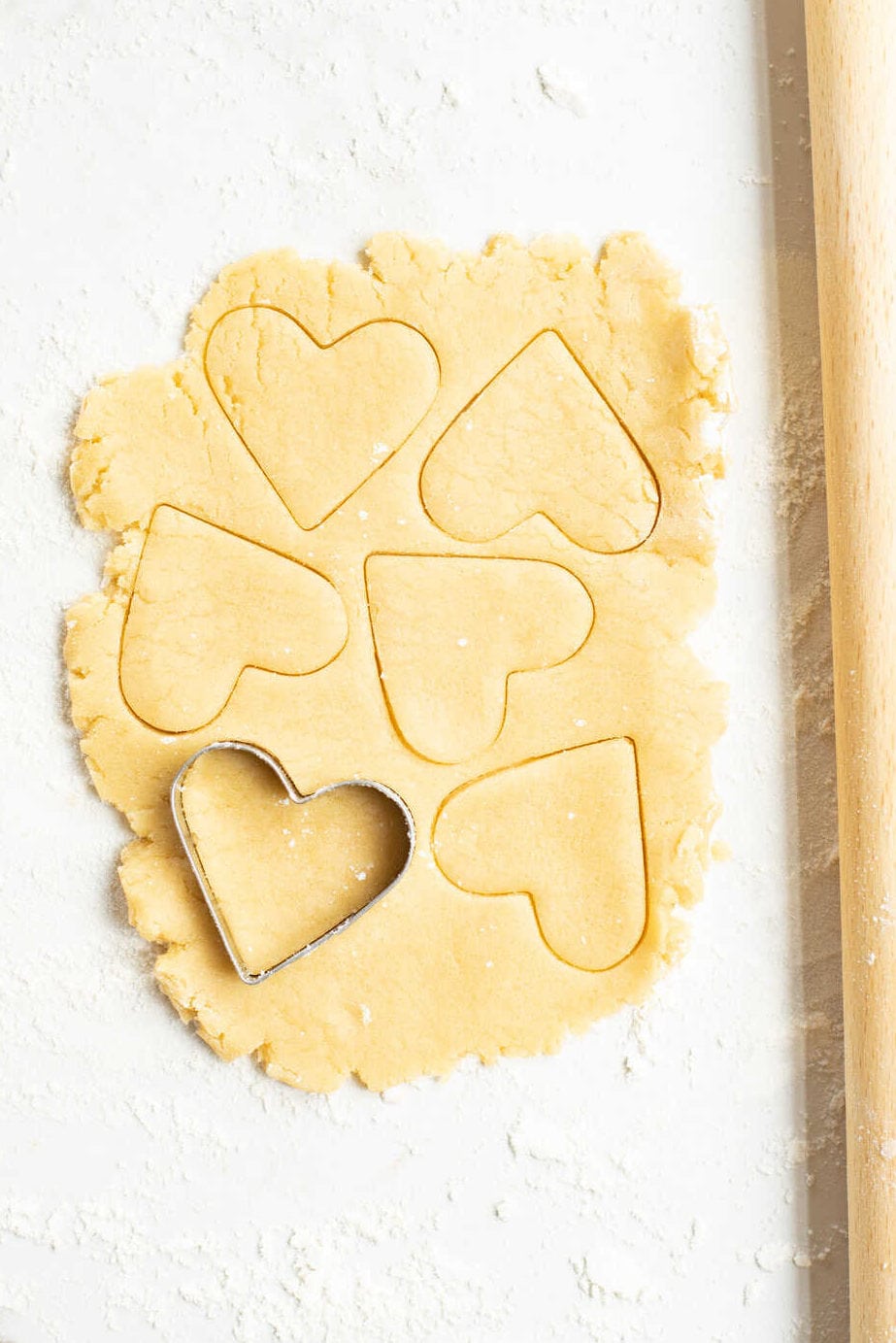 sugar cookie dough rolled out on a floured marble countertop with a heart-shaped cookie cutter.