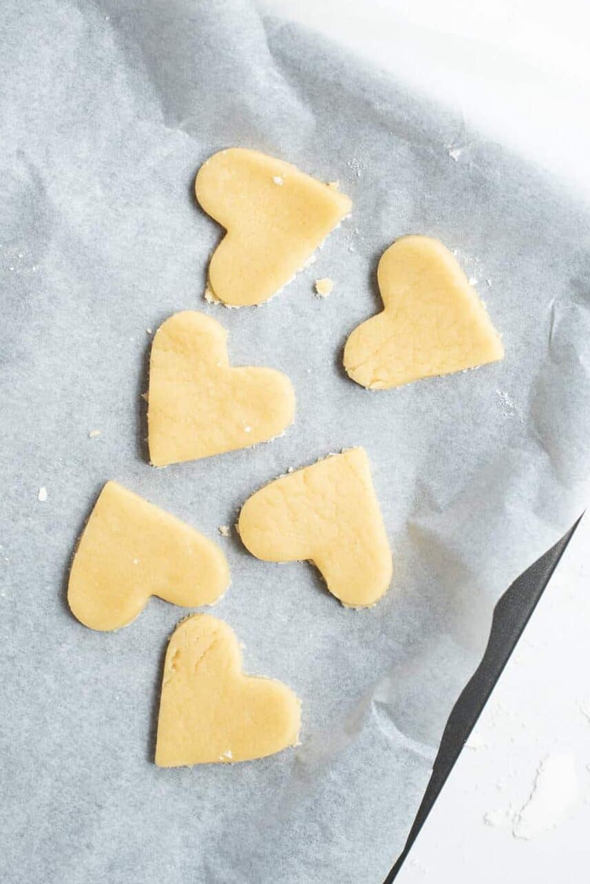 six heart-shaped sugar cookies arranged on a parchment-lined baking sheet.