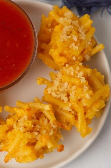 Mac and cheese bites on a plate next to a bowl of dip.