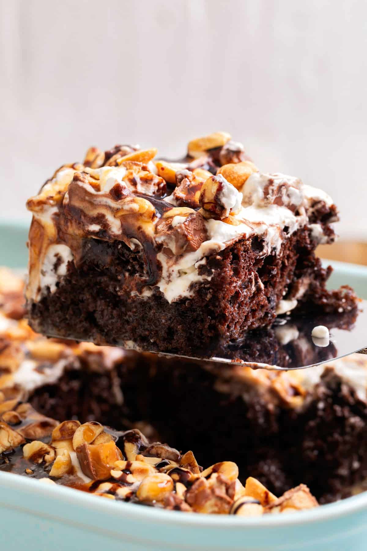 close up image of a square slice of snickers cake sitting on a metal cake spatula.