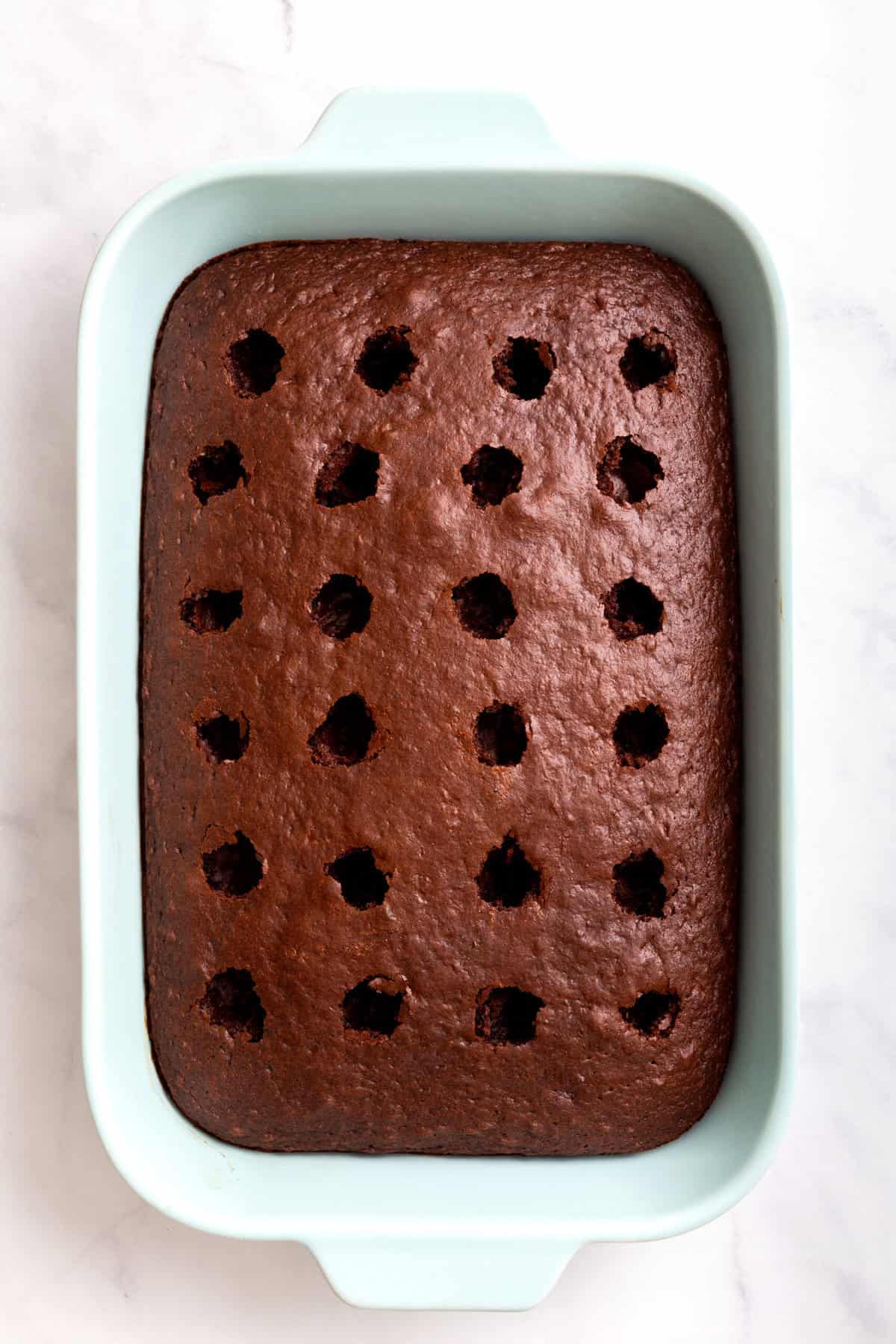 top down image of chocolate poke cake sitting in a light blue 9x13 casserole dish. 