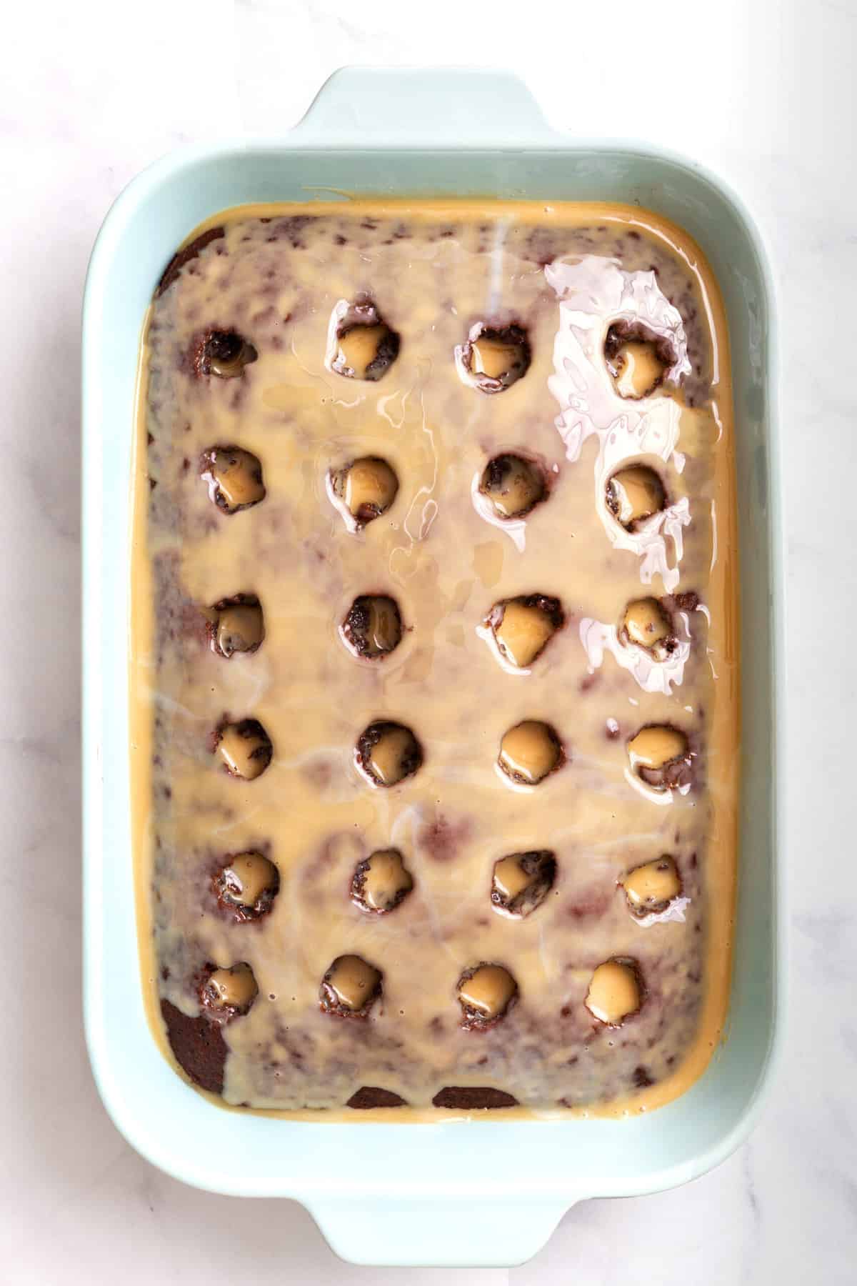 top down image of chocolate poke cake with sweetened condensed milk and caramel sauce poured over the top in a light blue 9x13 casserole dish. 