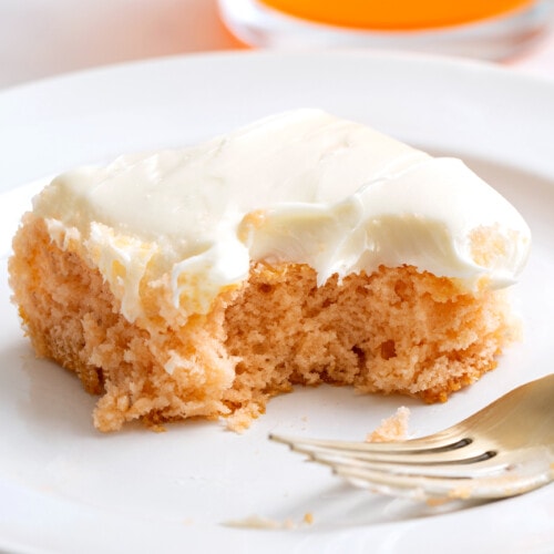 A slice of orange soda cake on a plate with a fork with a bite missing.