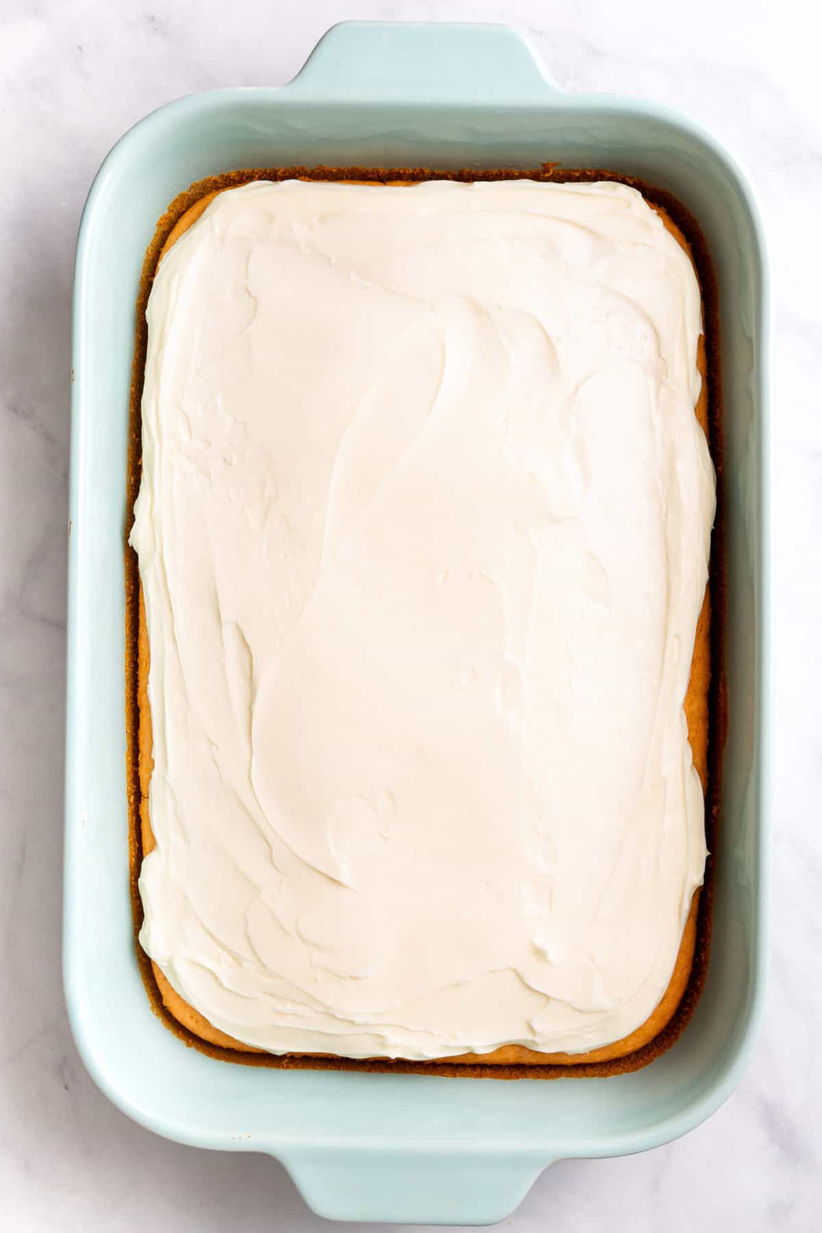 top down image of soda cake frosted sitting in a 9x13 casserole baking dish. 