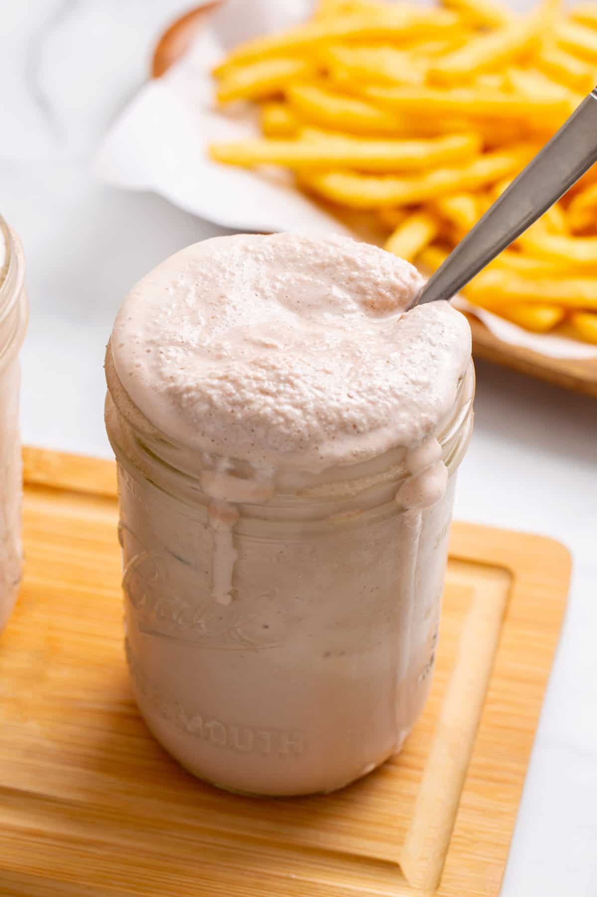 close up image of a mason jar of a homemade wendy's frosty with a silver spoon and sitting on a wood cutting board. 