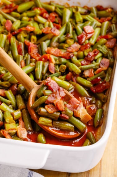 A spoon lifting a scoop of crack green beans from a baking dish.