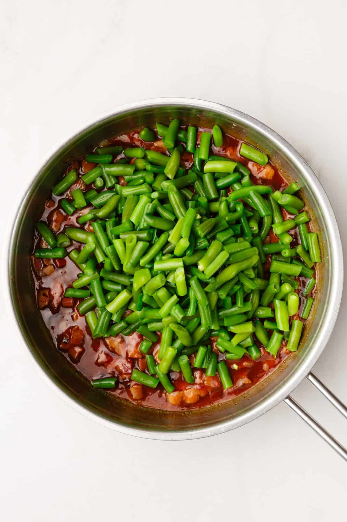 top down image of cooked bacon, onion and green beans sitting in a large skillet. 