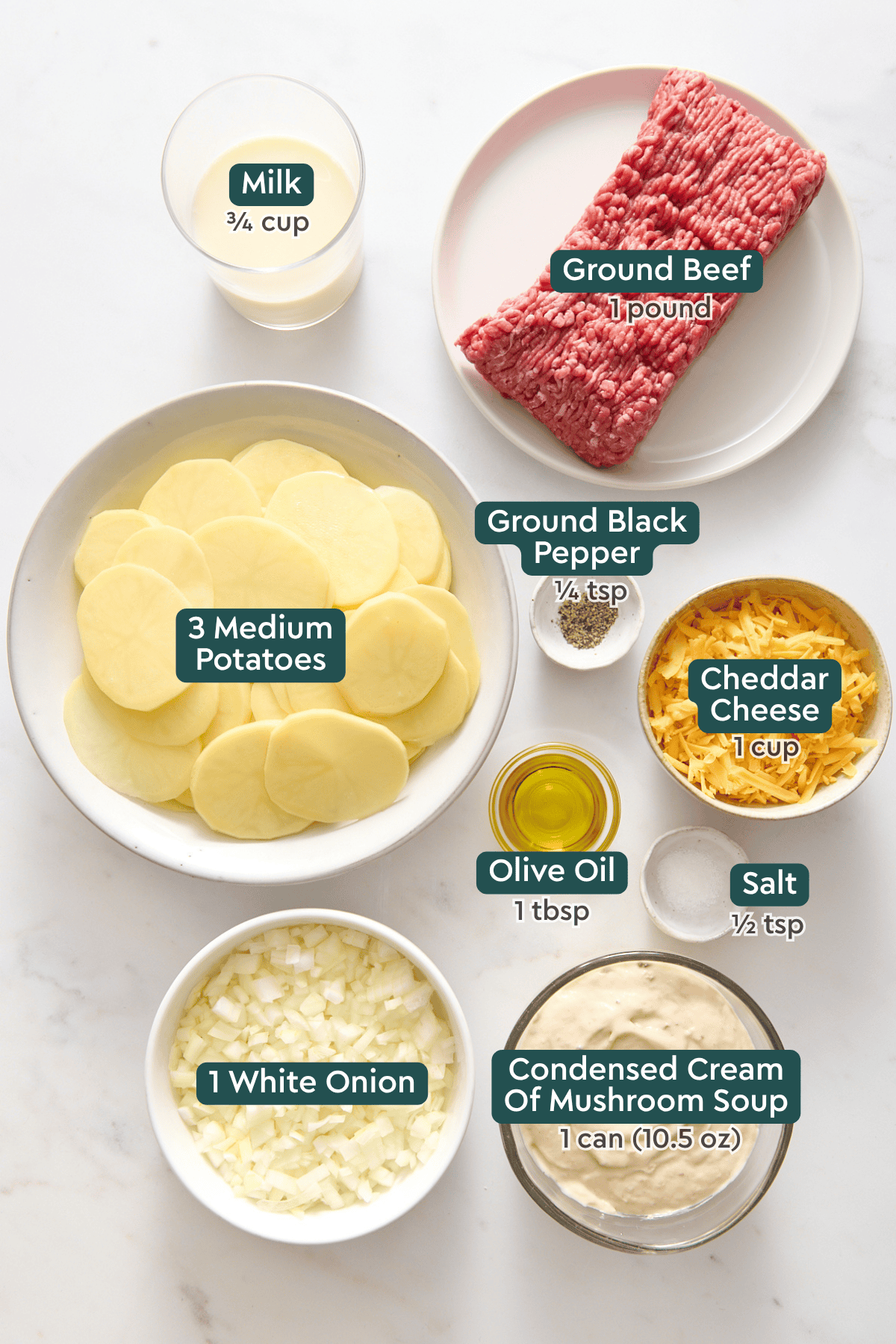 Ingredients for hamburger and potato casserole, including milk, ground beef, potatoes, cheddar, oil, pepper, salt, onion, cream of mushroom soup.