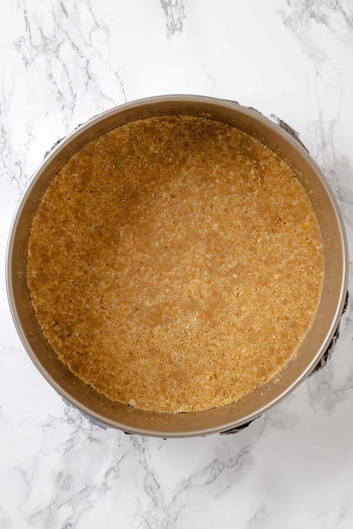 top down image of homemade graham cracker crust pressed in a springform pan. 