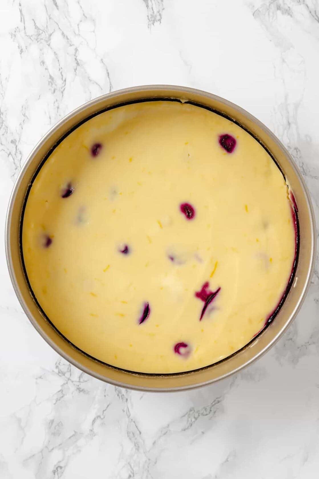 top down image of baked homemade Lemon Blueberry Cheesecake sitting in a springform pan. 