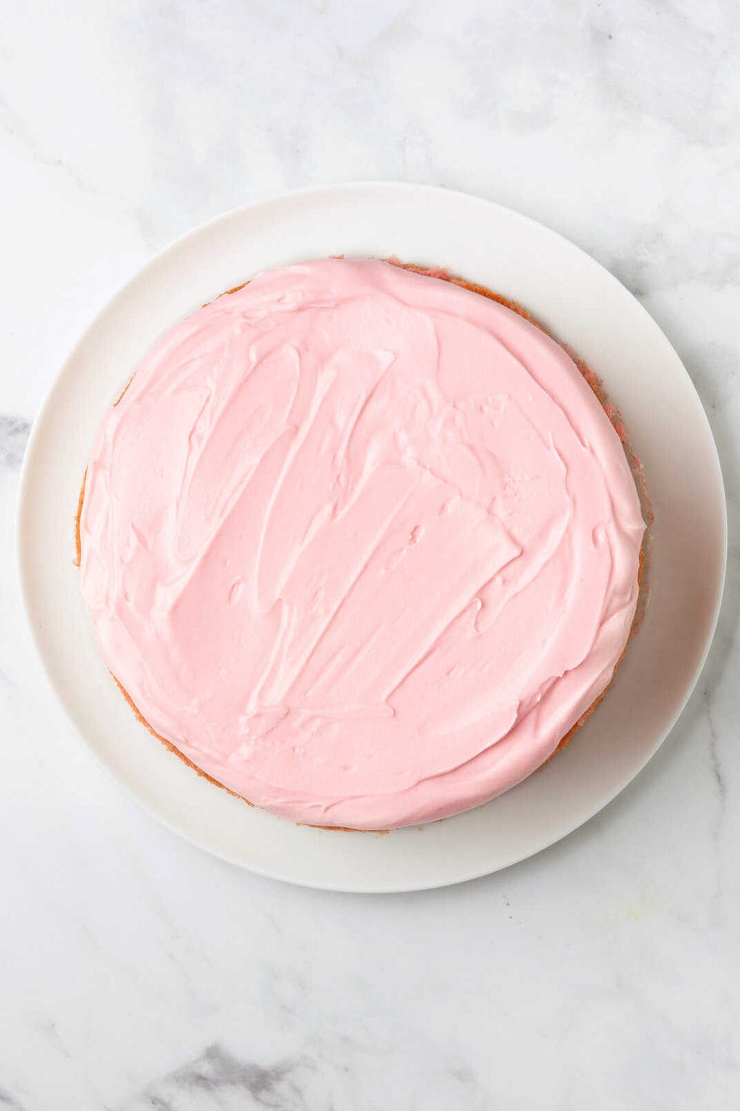 top down image of strawberry frosted cake sitting on a white round plate. 