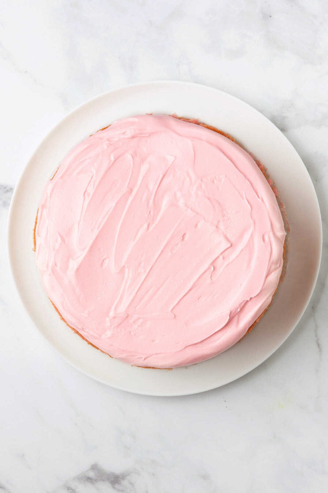 top down image of strawberry frosted cake sitting on a white round plate.