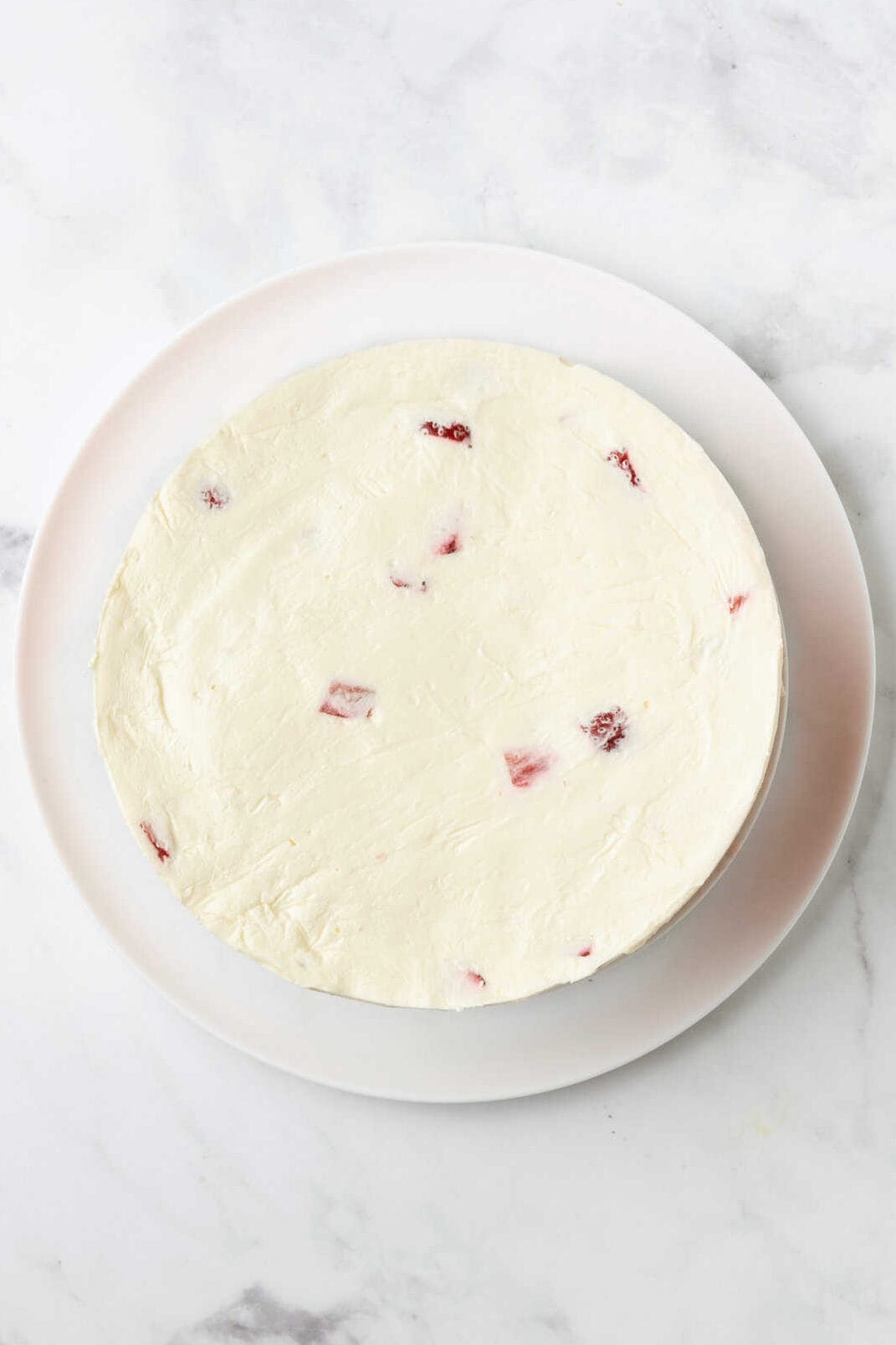 top down image of strawberry ice cream cake sitting on a white round plate. 